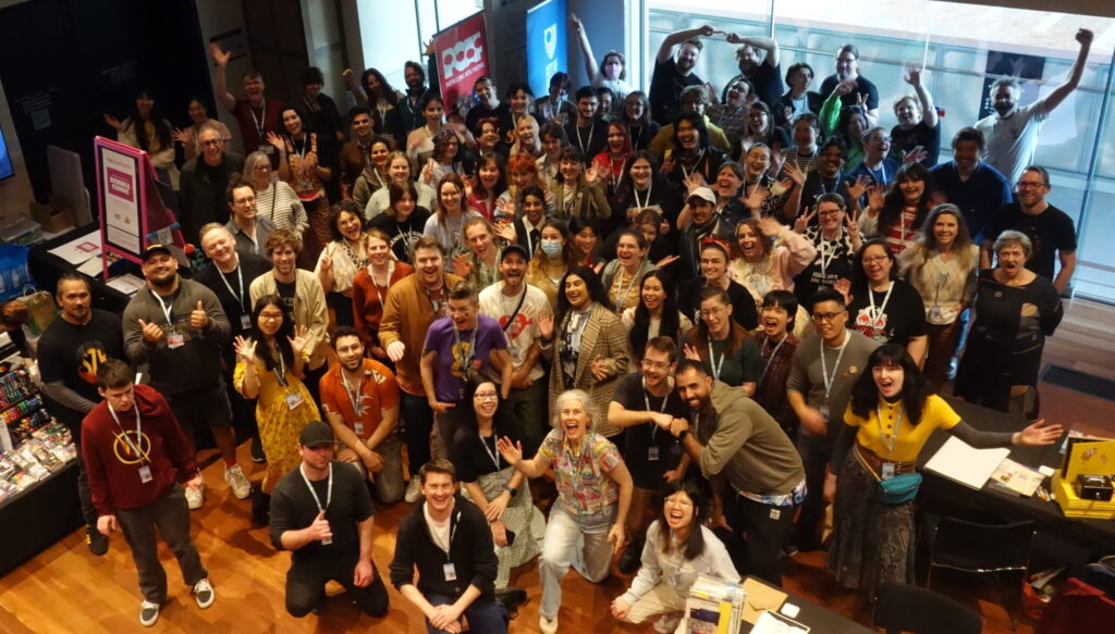 Crowd of about eighty comic makers who exhibited at the 2023 PCAF Market Hall cheering at the camera.